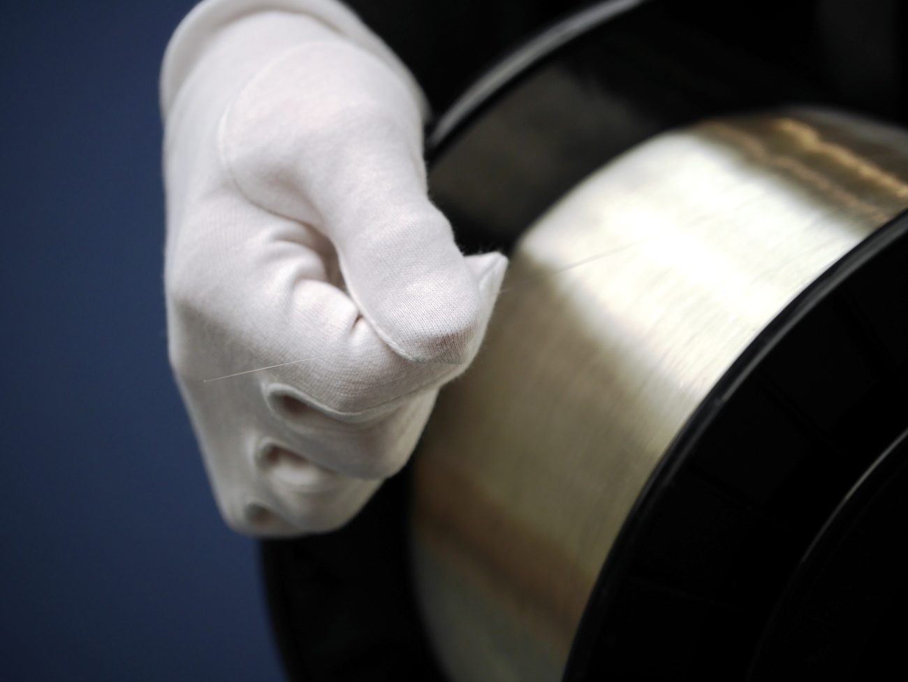A hand is wearing a white glove and is holding the end of an optical fiber, rolled up on a spool.