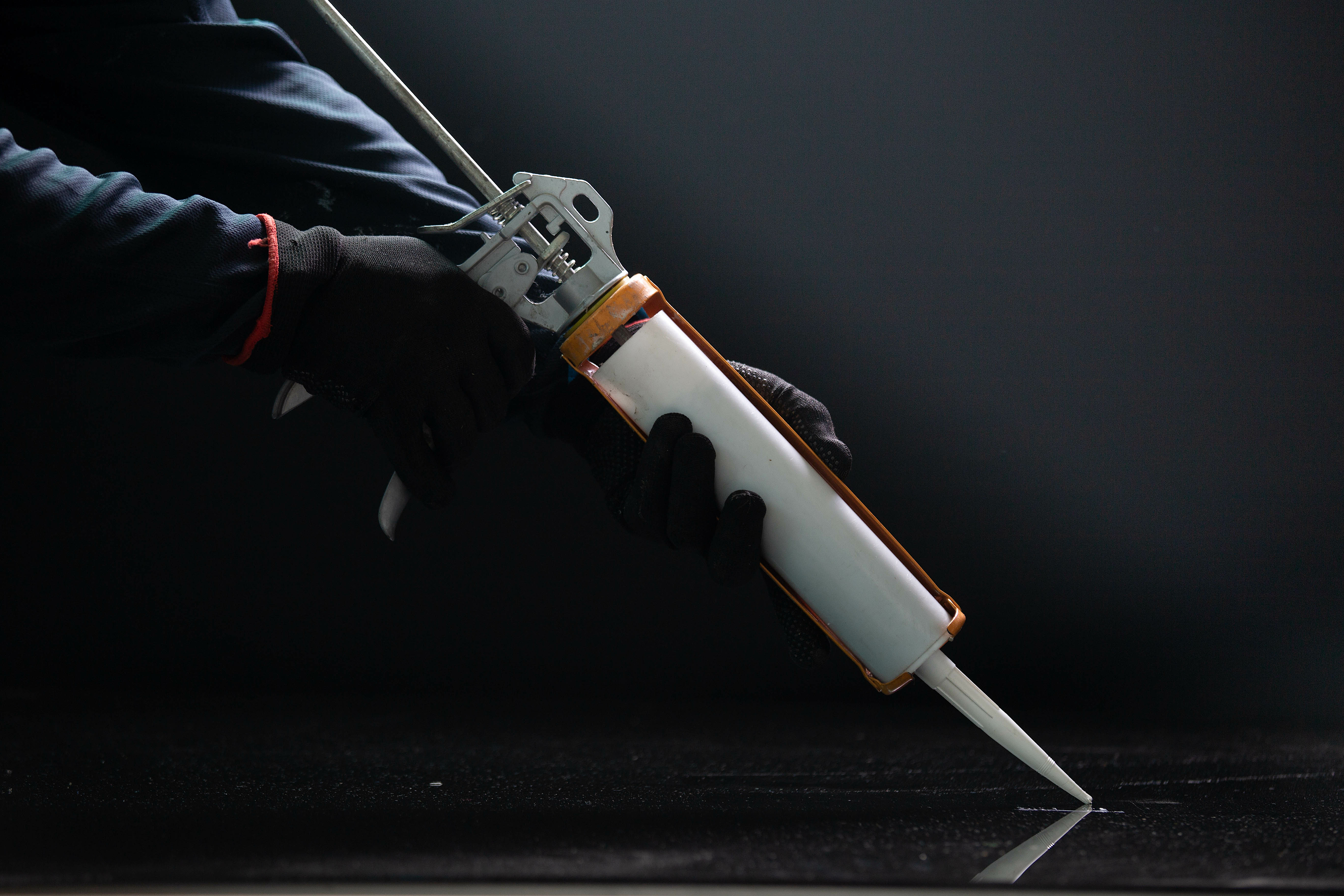 Two hands wearing black gloves are holding a silicone syringe that is placed on a surface. The background is black. 