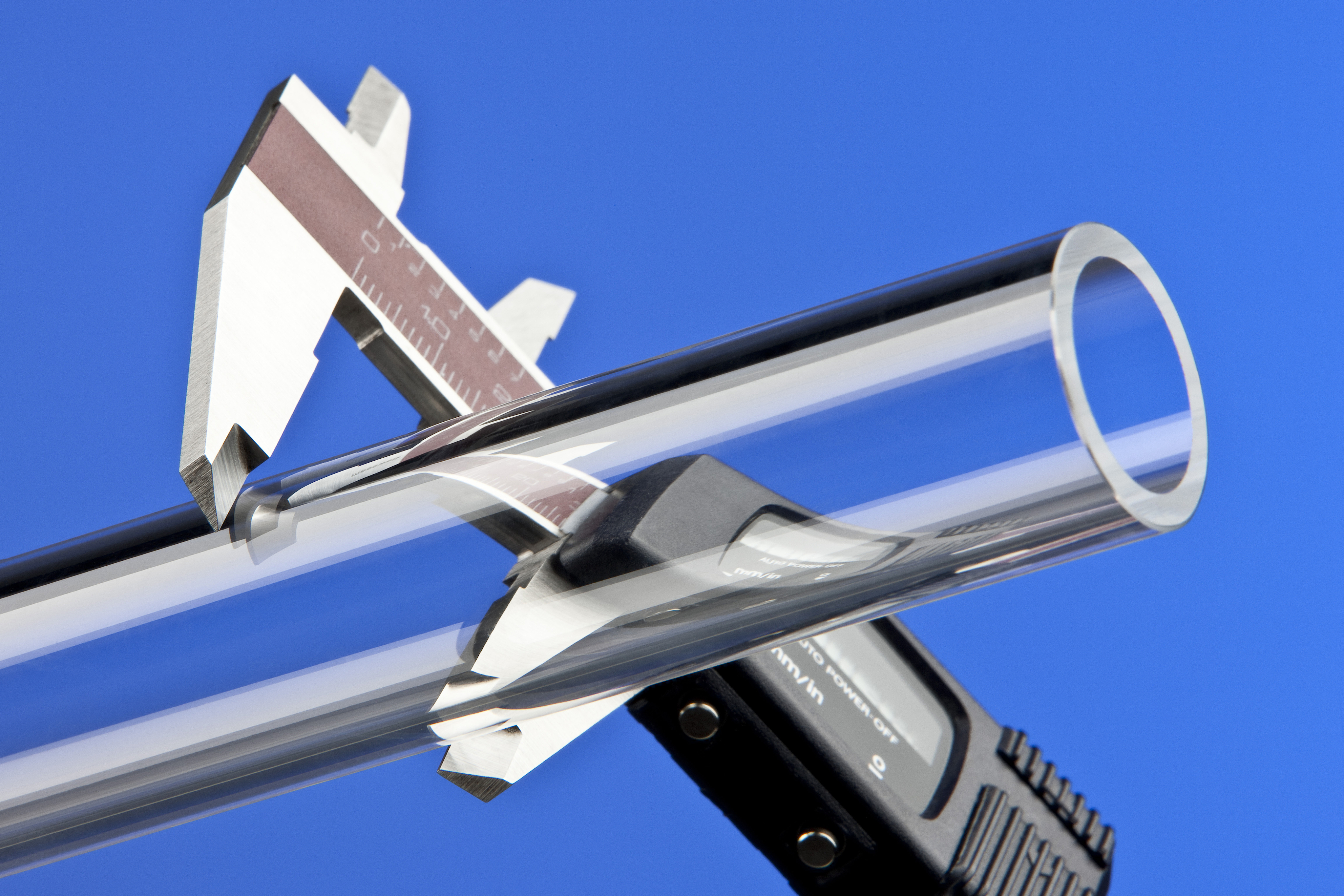 A glass tube is measured with a caliper gauge; the background is blue. 