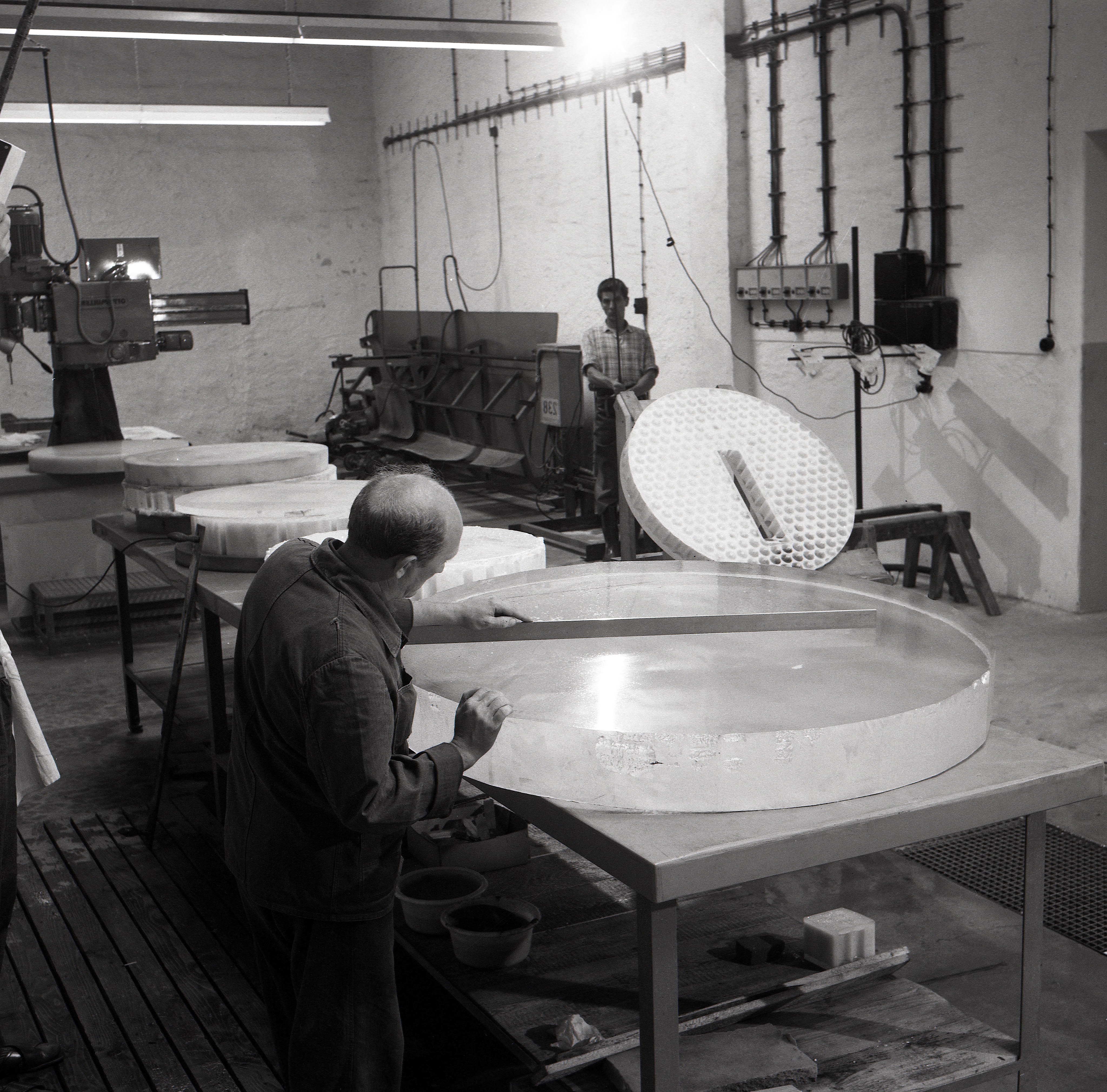 Old black and white photo: production hall with 2 people processing glass panes. 
